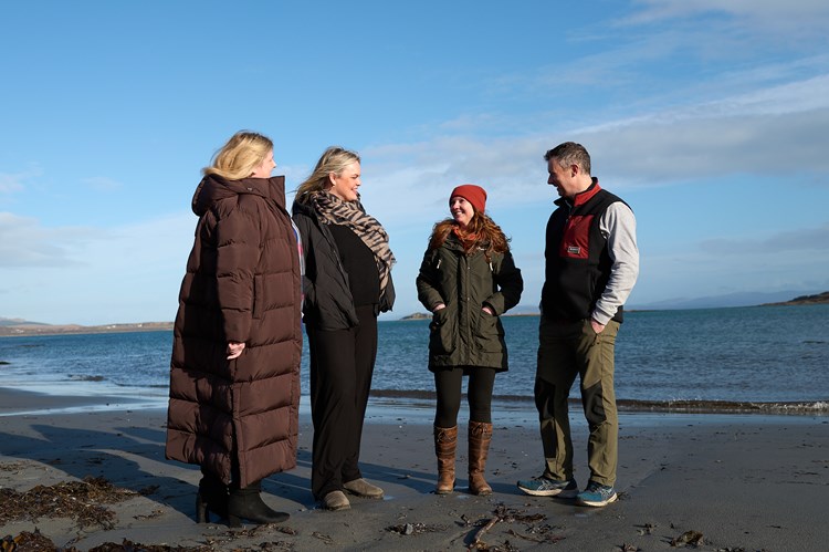 a group of people wearing winter coats and having a conversation on the beach