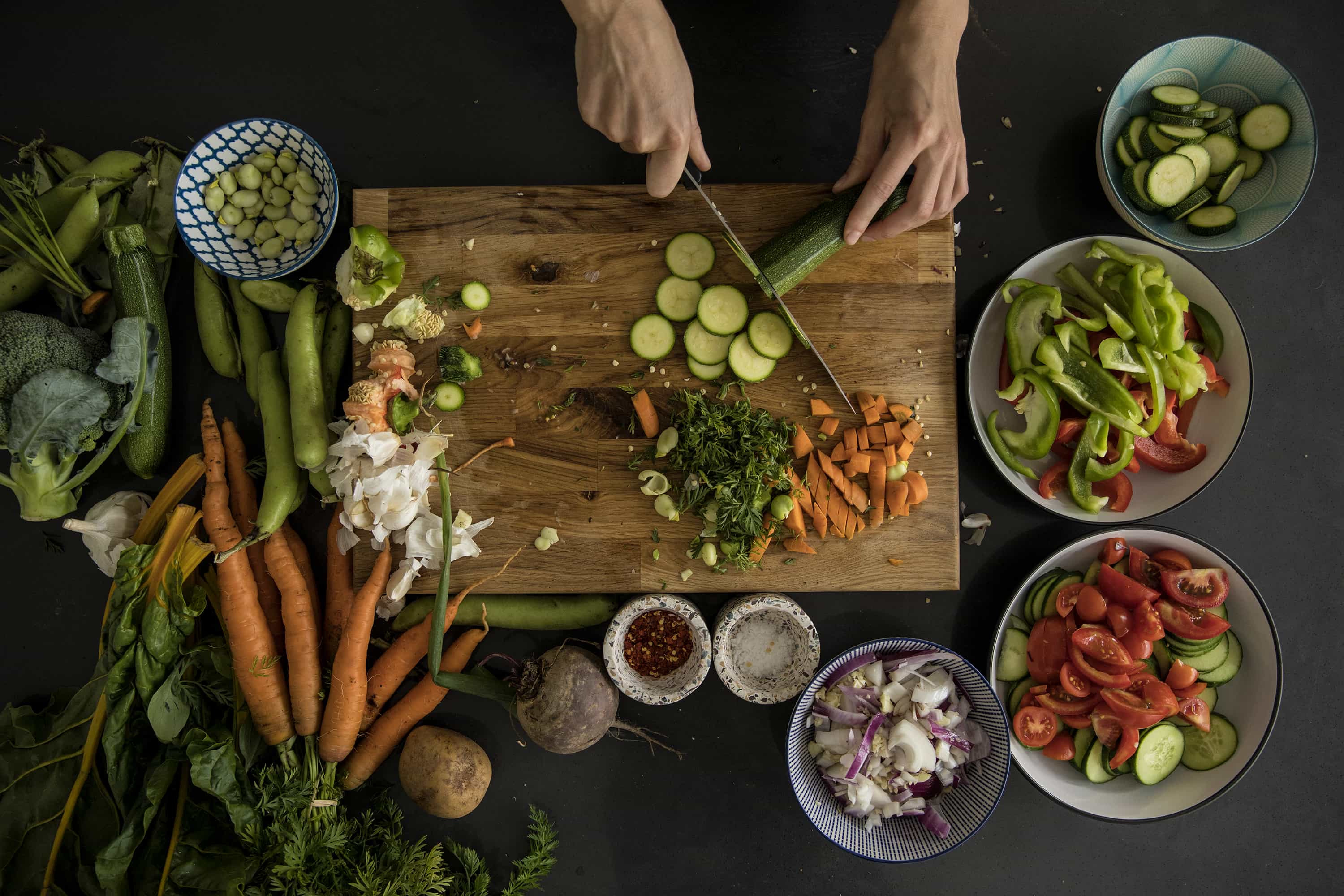 A person chopping raw vegetables on a wooden chopping board