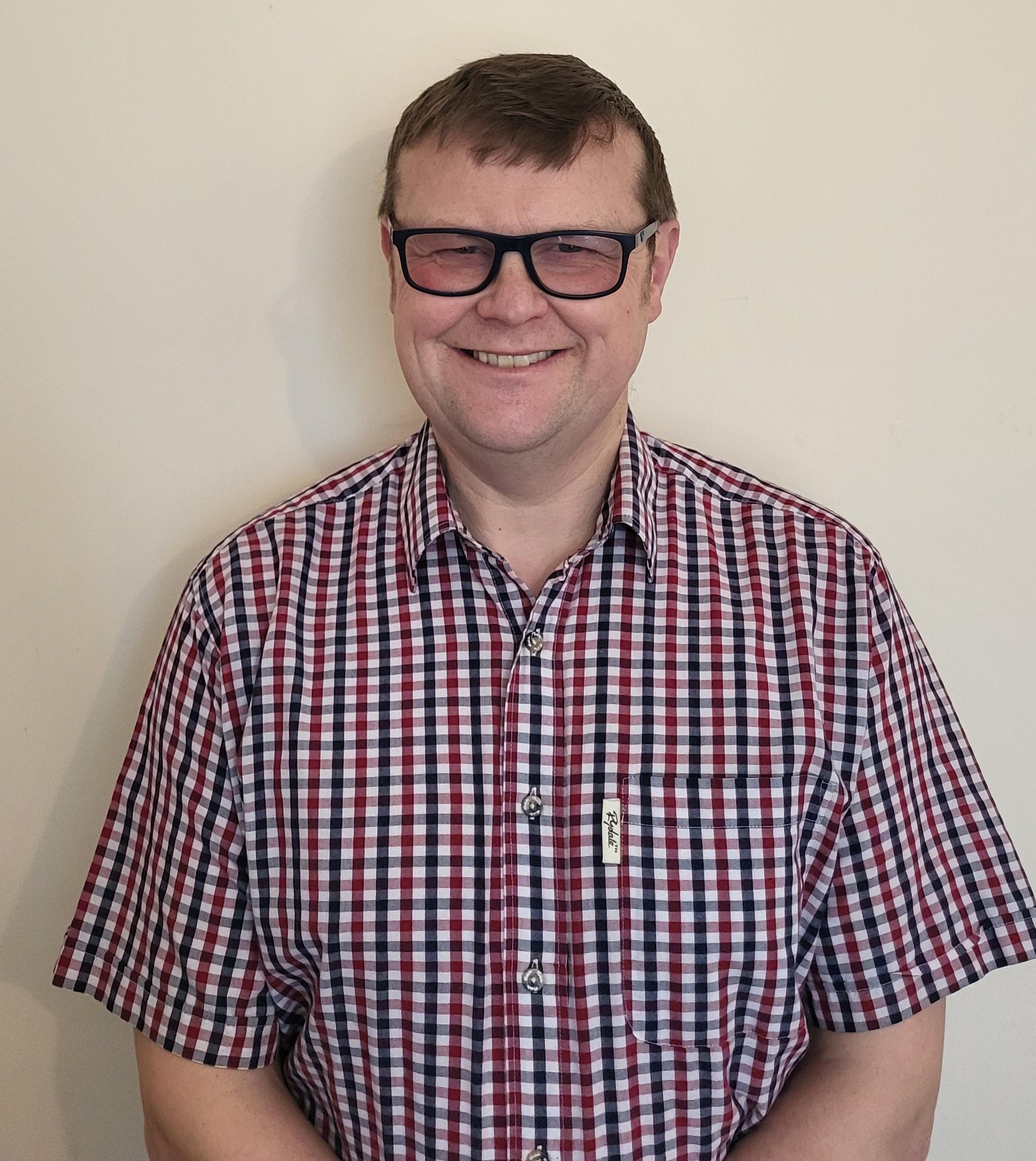 A man wearing a checked shirt and smiling