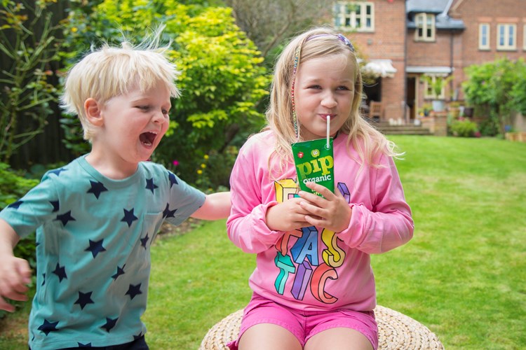 Two children in a garden, a boy and a girl - the girl is drinking a Pip Organic apple juice box