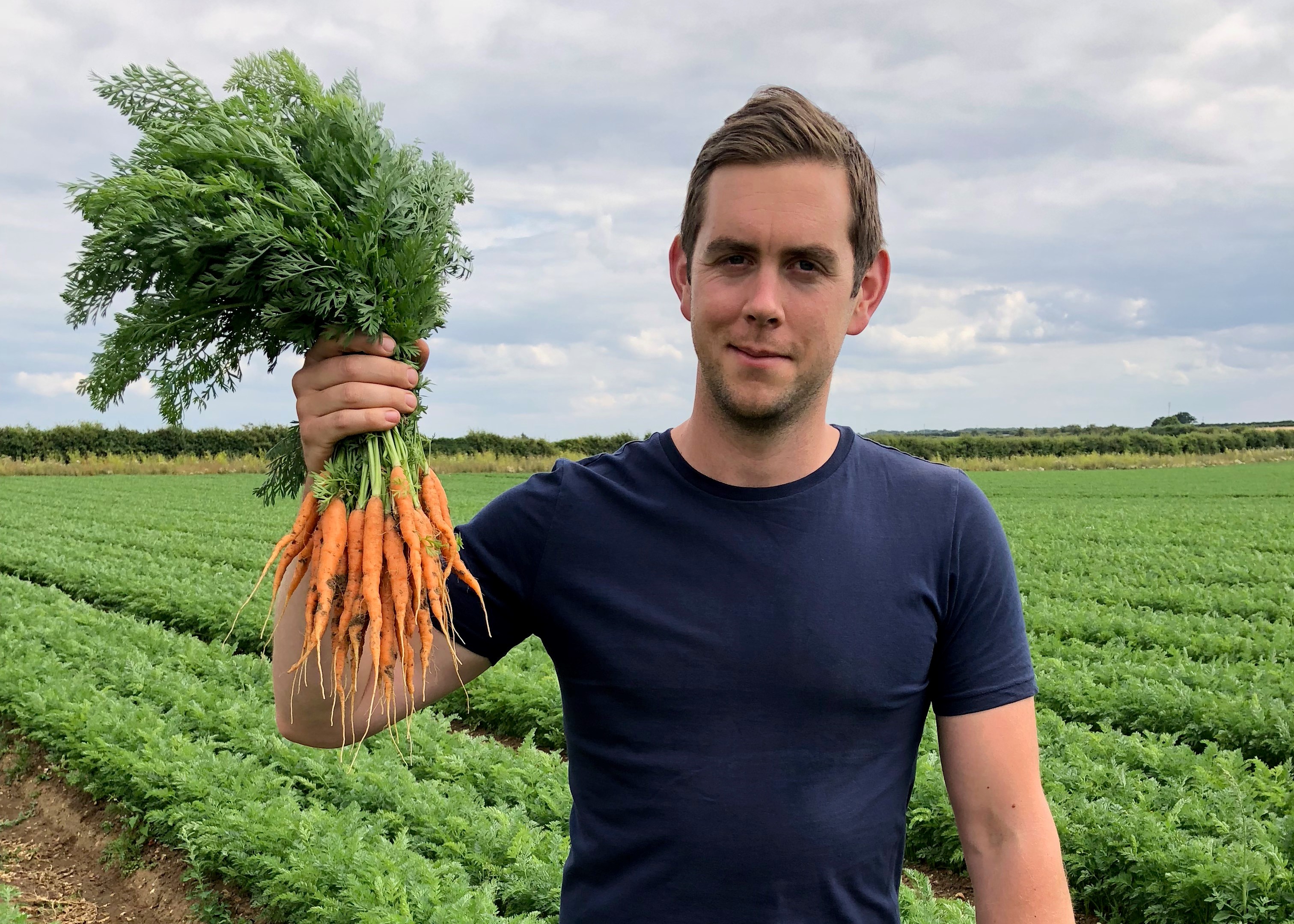 joe in a field holding a bunch of carrots