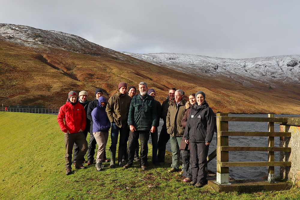 Group of people posing in front of snowy mountain tops and lake. 