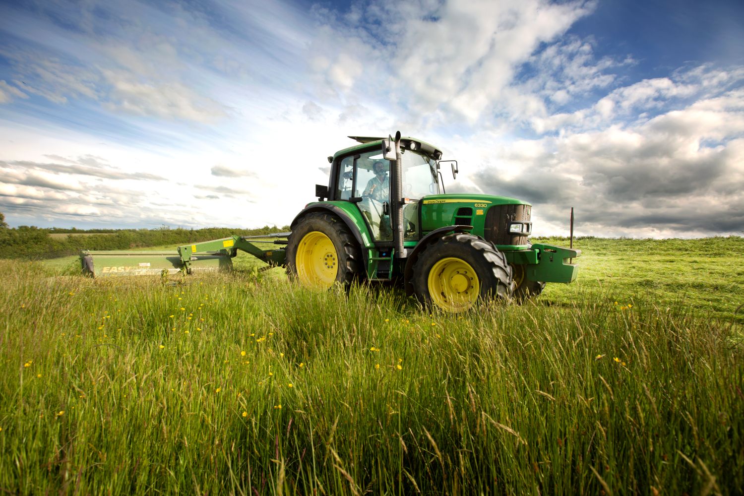 A tractor cutting silage in a meadow full of grass and flowers