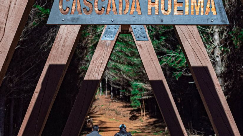 Two people walking past a sign for Cascada Hueima
