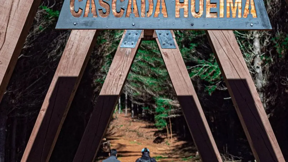 Two people walking past a sign for Cascada Hueima