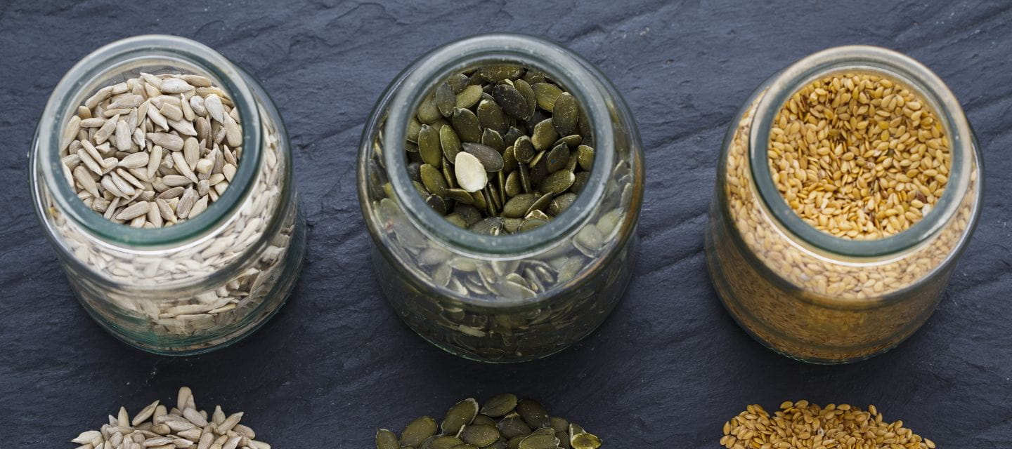 Three jars displaying sunflower, pumpkin and sesame seeds on a slate surface