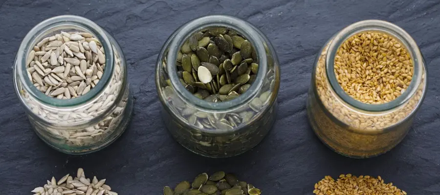 Three jars displaying sunflower, pumpkin and sesame seeds on a slate surface
