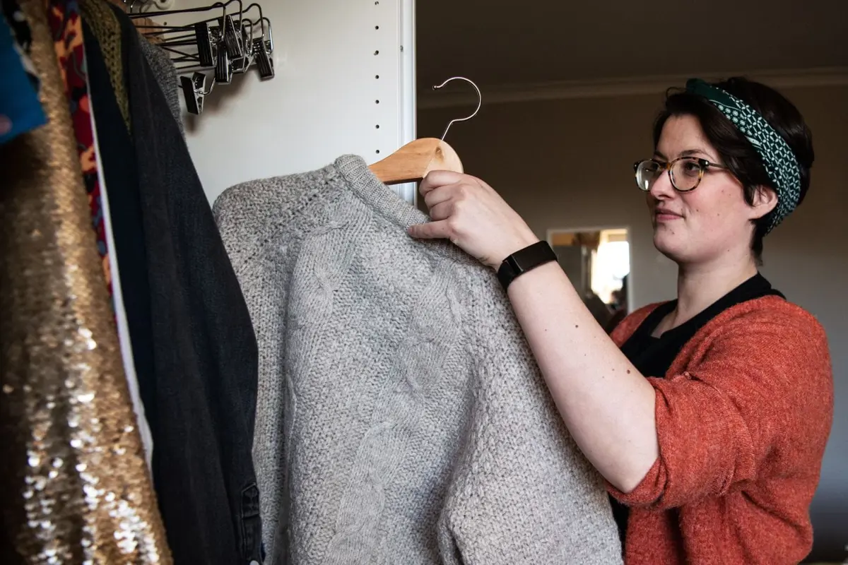 A woman wearing glasses putting a knitted jumper away in a wardrobe
