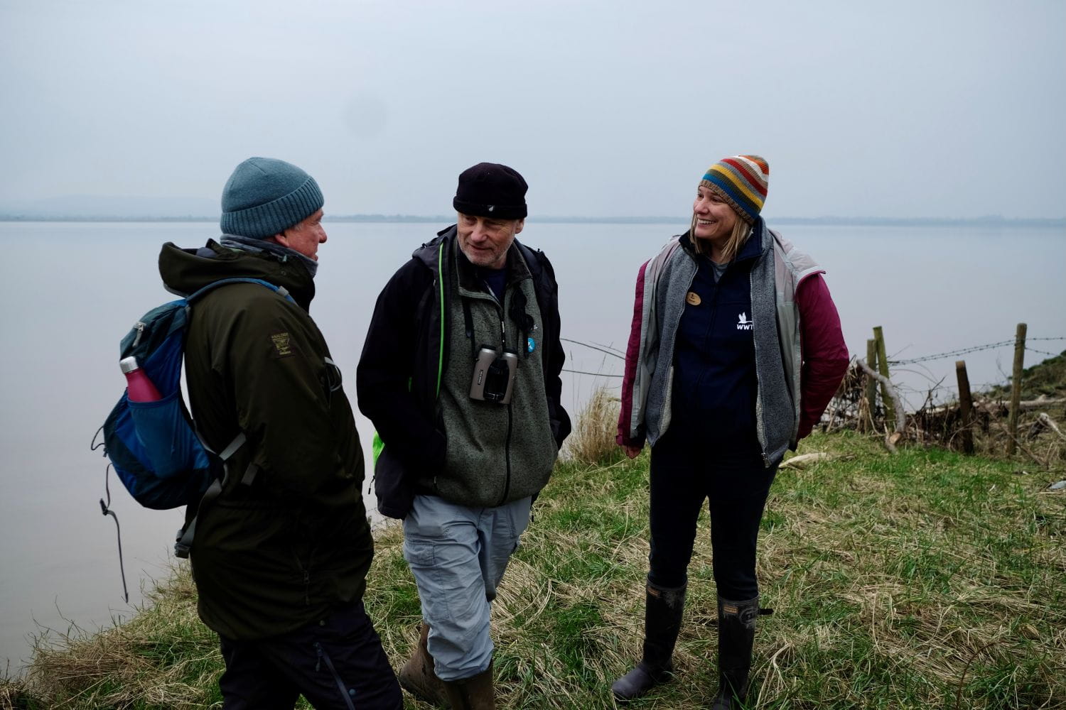 Three people talking outside with a large body of water behind them