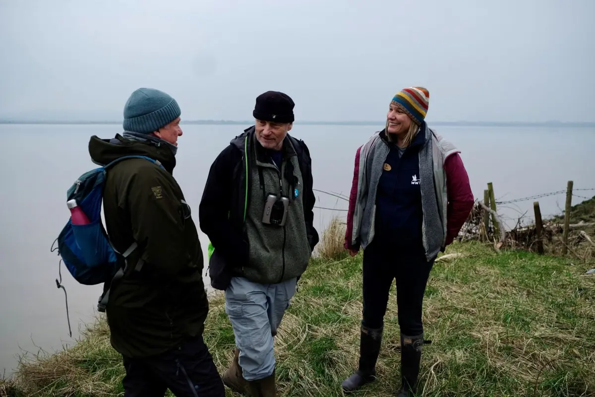 Three people talking outside with a large body of water behind them