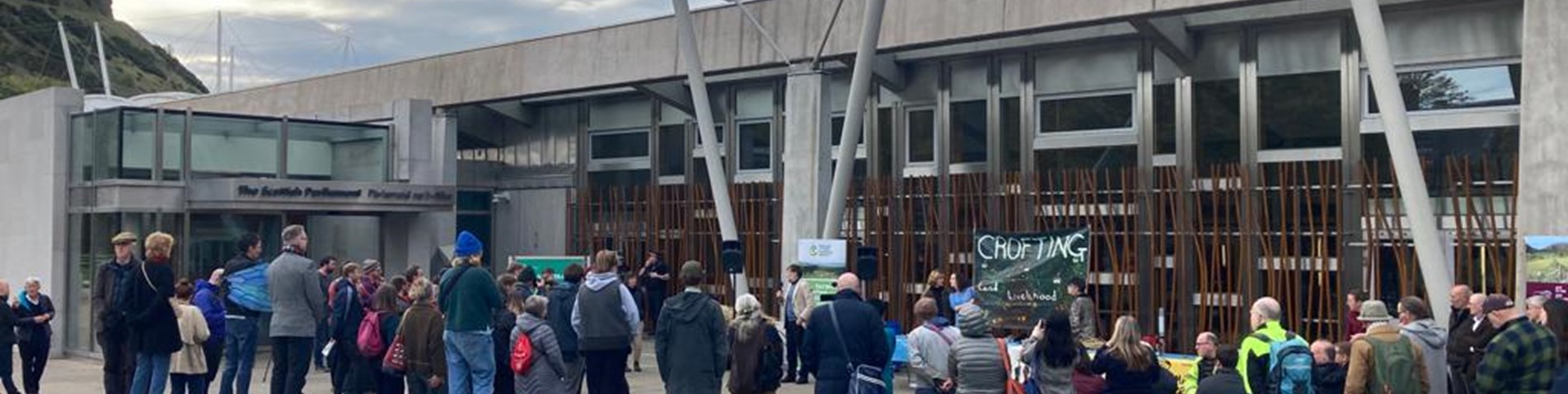 A group of people listening to a speaker outside the Scottish parliament building