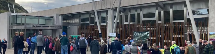 A group of people listening to a speaker outside the Scottish parliament building
