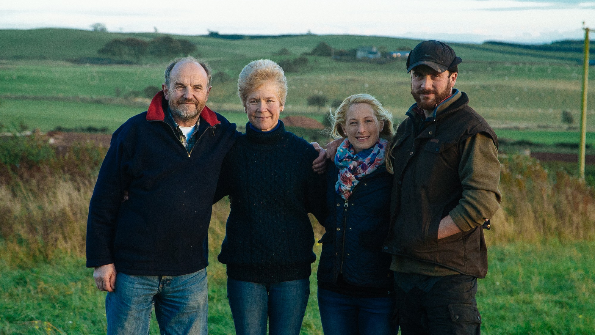 Walton family of Peelham farm pose smiling with fields behind them. 
