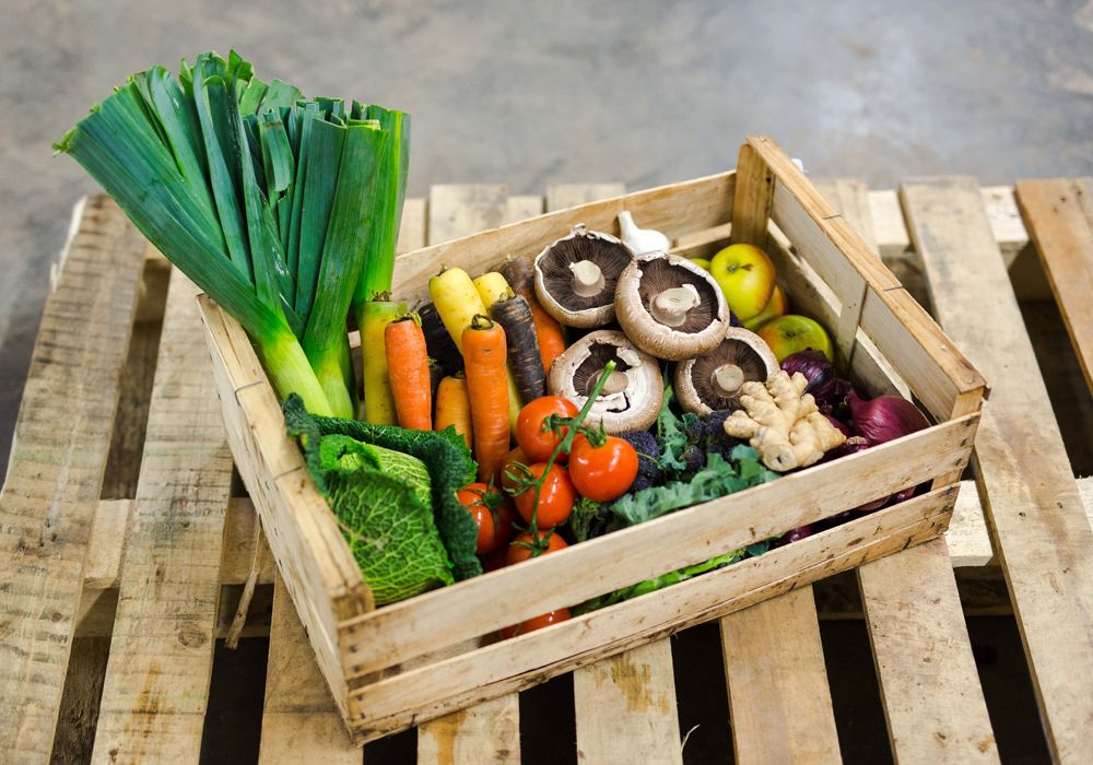 A wooden vegetable box full of different fruits and vegetables