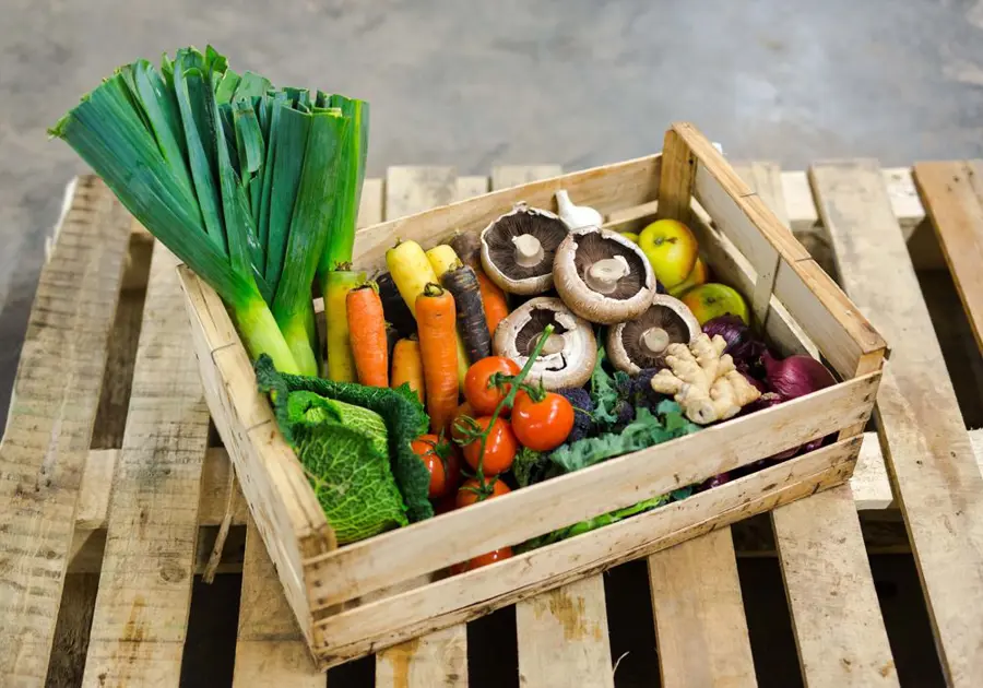 A wooden vegetable box full of different fruits and vegetables