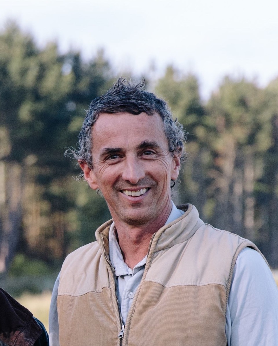 A man smiling and standing in front of a wooded area