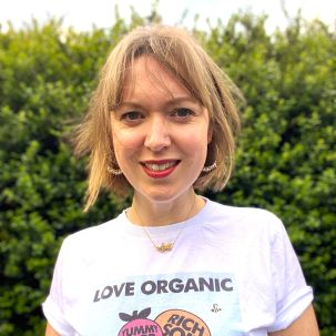 A woman with a choppy bob wearing red lipstick, hoop earrings and a t-shirt that says Love Organic