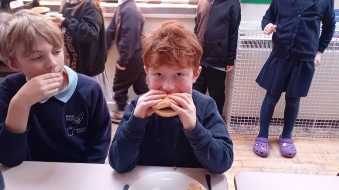Child looks into camera while taking bite of wild venison burger in a roll. 