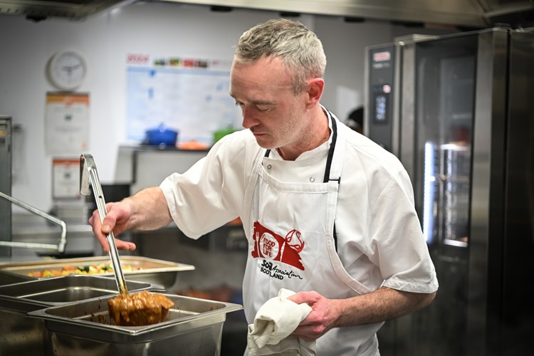 A chef ladling food from a bain marie