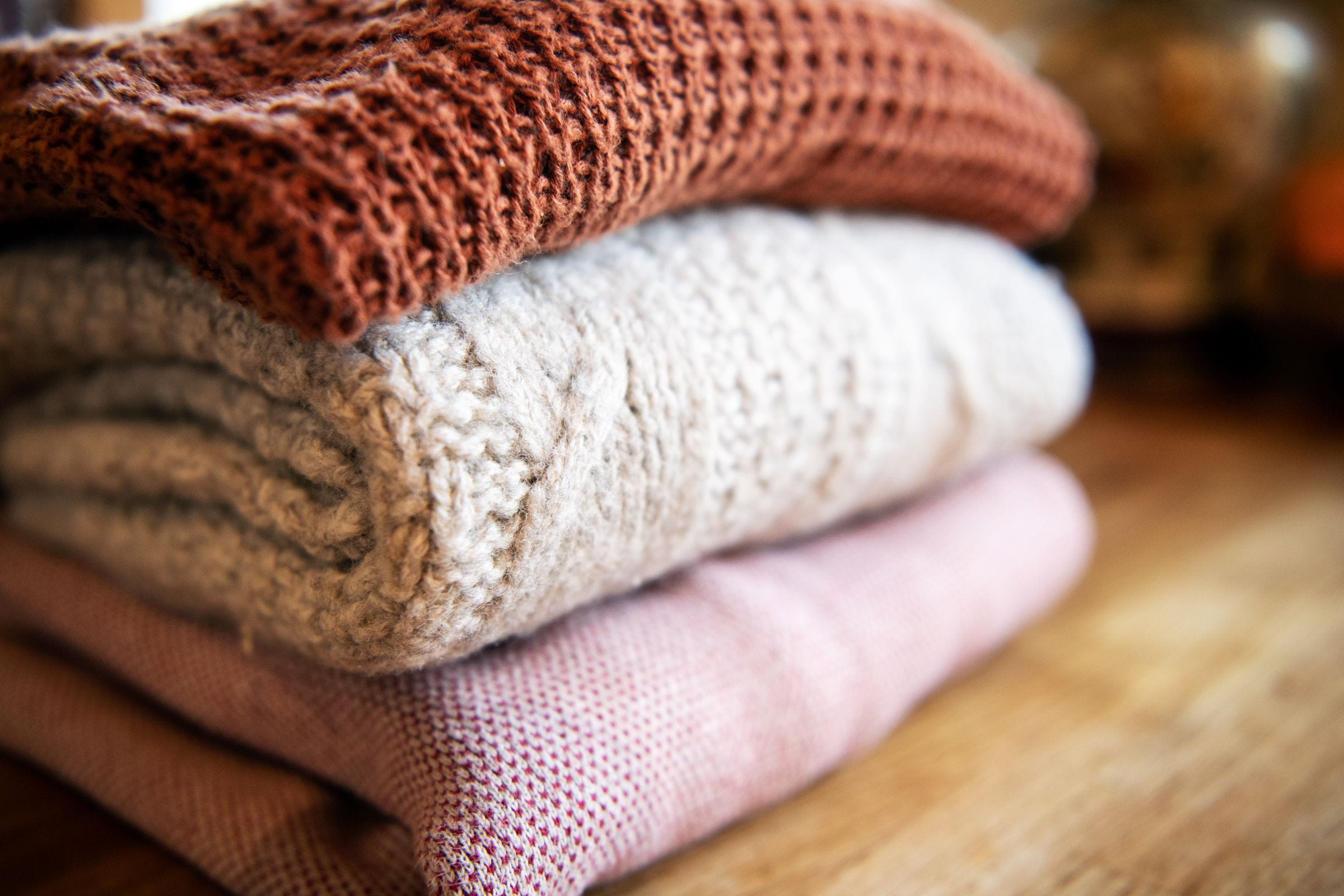 Three folded sweaters on a wooden table