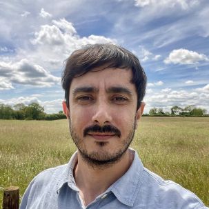 A man with dark hair and facial hair standing in a field