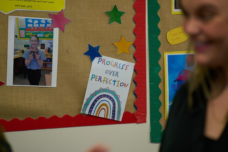 a school noticeboard with a picture of a child and a card reading progress over perfection