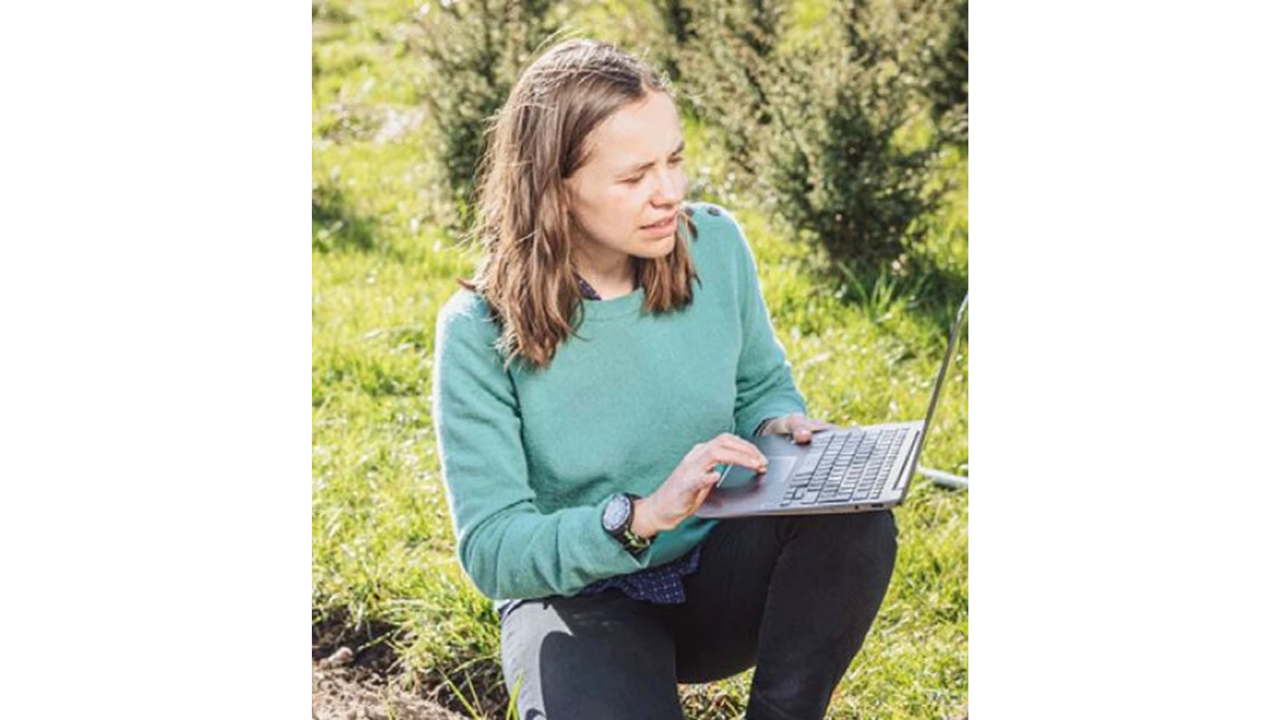 Ichsani Wheeler, OpenGeoHub Foundation kneeling in a field with one hand using the touchpad of a laptop