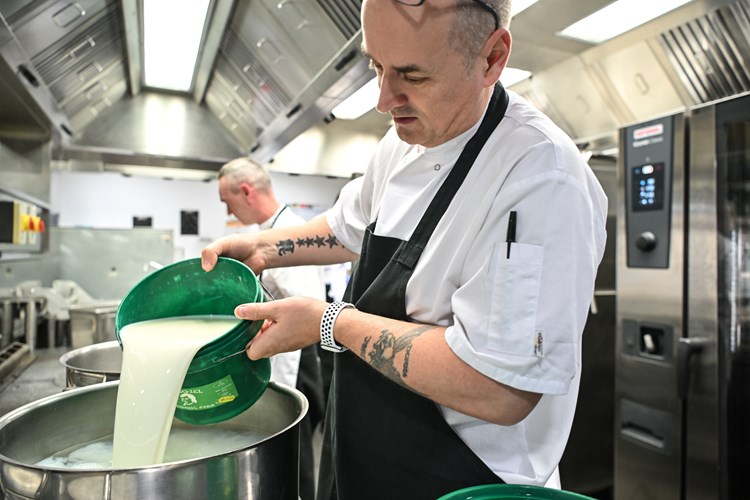 A chef pouring milk into a large saucepan